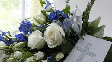 Blumenarrangement mit weißen Rosen und blauen Blüten, kombiniert mit einer tiefen Karte mit gekreuztem Motiv.