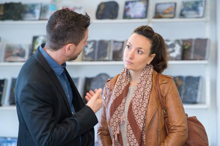 Zwei Personen im Gespräch in einem Geschäft, im Hintergrund sind verschiedene Produkte auf Regalen sichtbar.